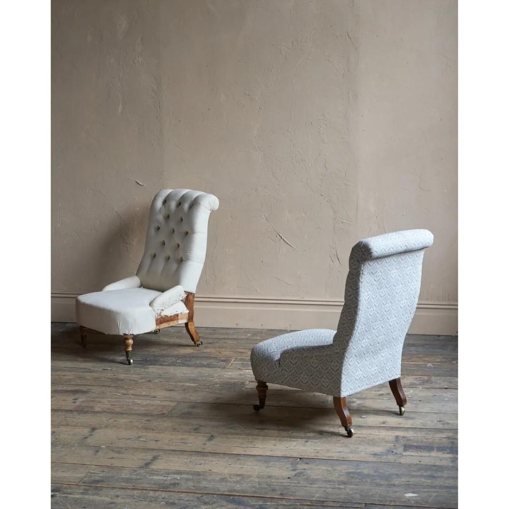 A pair of low Victorian button-back armchairs with turned wooden legs and brass castors, one in calico and one in patterned grey fabric. View IV