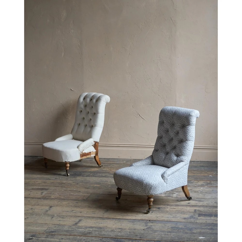 A pair of low Victorian button-back armchairs with turned wooden legs and brass castors, one in calico and one in patterned grey fabric. View V