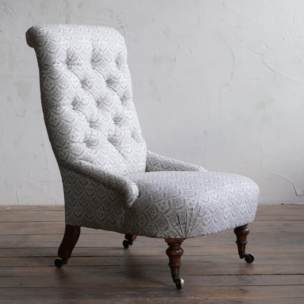 A pair of low Victorian button-back armchairs with turned wooden legs and brass castors, one in calico and one in patterned grey fabric. View VII