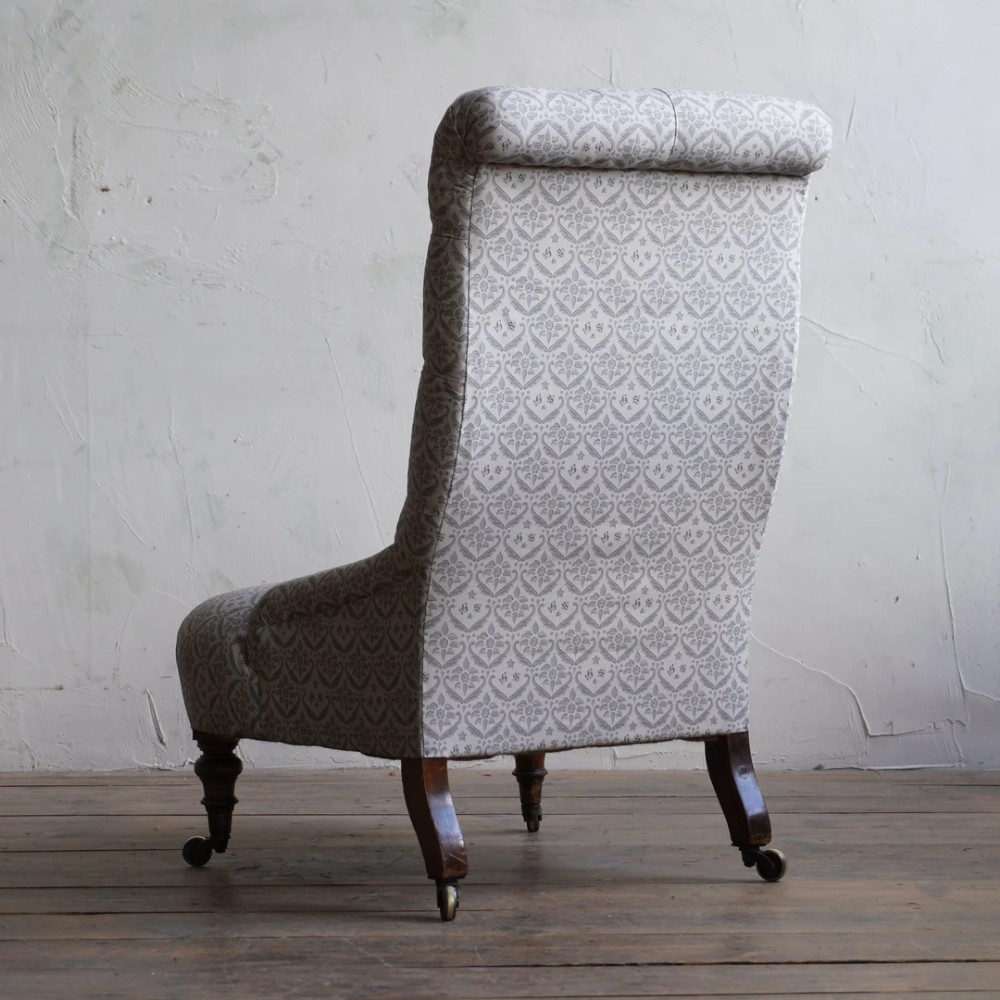 A pair of low Victorian button-back armchairs with turned wooden legs and brass castors, one in calico and one in patterned grey fabric. View X
