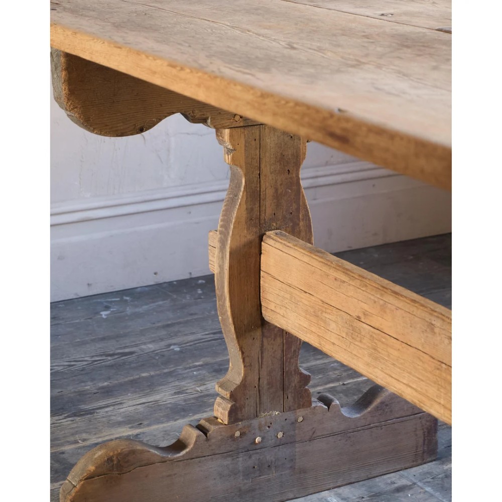 An 18th-century Swedish pine dining table featuring a rectangular plank top resting on a sculpted trestle base with a central stretcher. View XII
