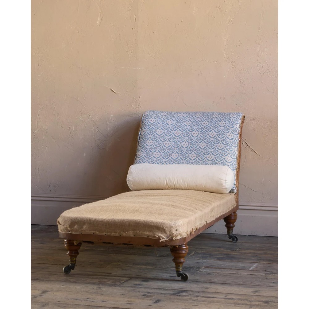A 19th-century upholstered chaise longue with turned wooden legs on brass castors, patterned fabric backrest, hessian base, and cream bolster cushion.