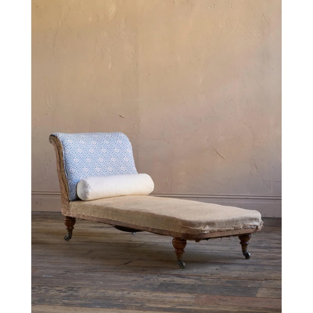 A 19th-century upholstered chaise longue with turned wooden legs on brass castors, patterned fabric backrest, hessian base, and cream bolster cushion. View II