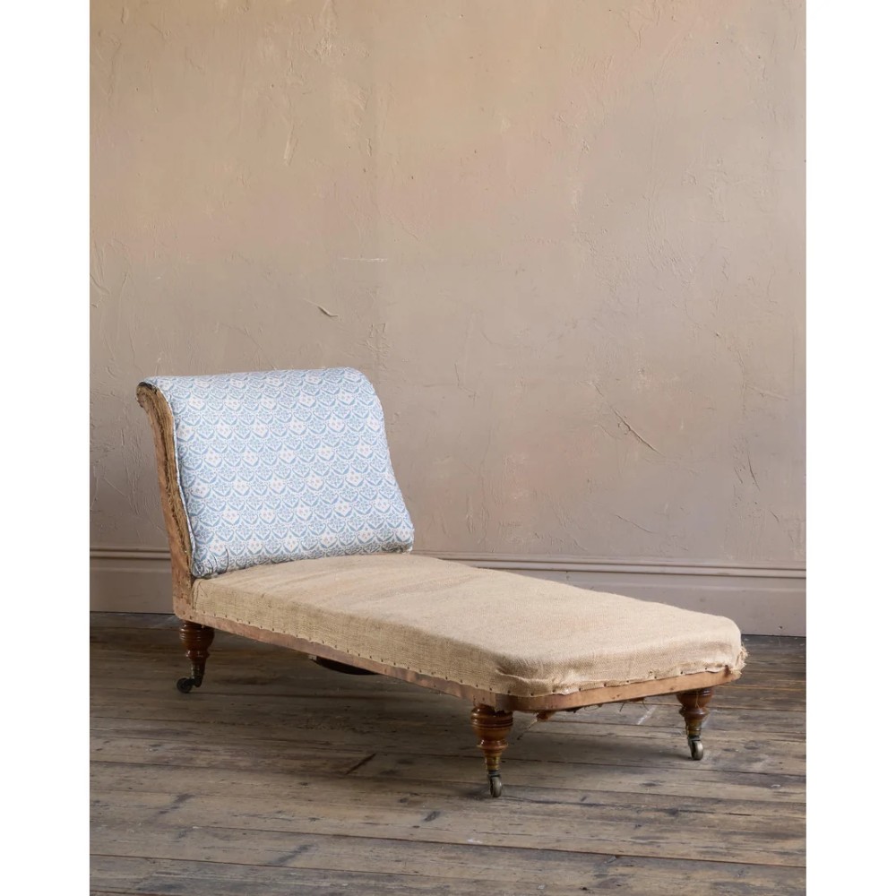 A 19th-century upholstered chaise longue with turned wooden legs on brass castors, patterned fabric backrest, hessian base, and cream bolster cushion. View IV