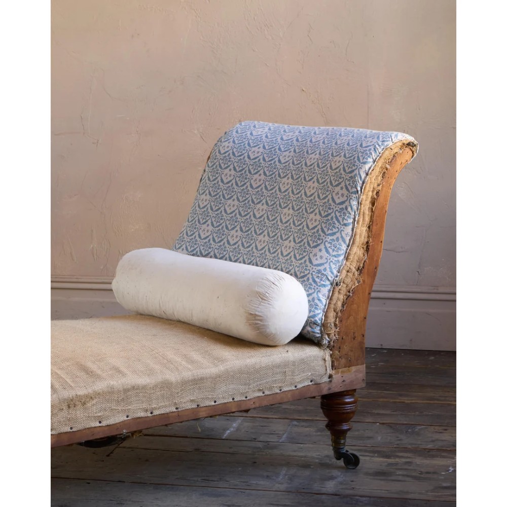 A 19th-century upholstered chaise longue with turned wooden legs on brass castors, patterned fabric backrest, hessian base, and cream bolster cushion. View VI