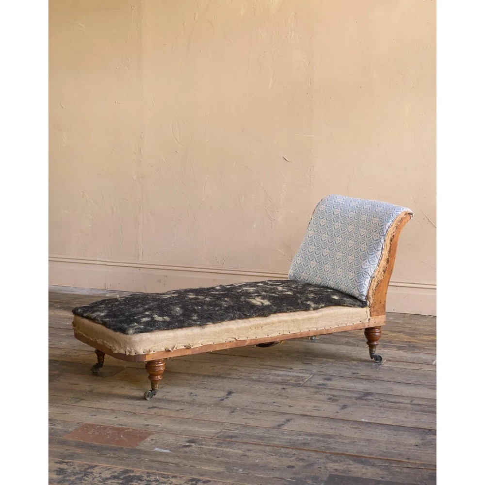 A 19th-century upholstered chaise longue with turned wooden legs on brass castors, patterned fabric backrest, hessian base, and cream bolster cushion. View VII