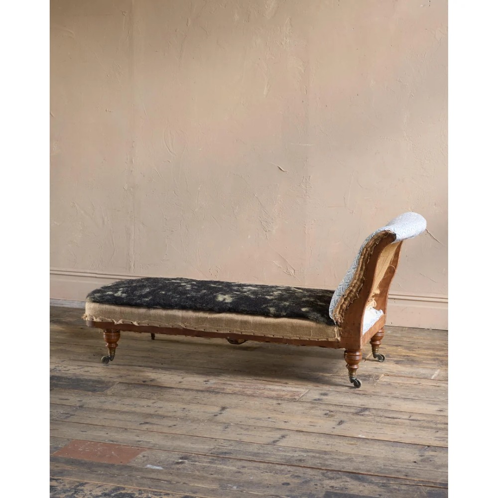 A 19th-century upholstered chaise longue with turned wooden legs on brass castors, patterned fabric backrest, hessian base, and cream bolster cushion. View VIII