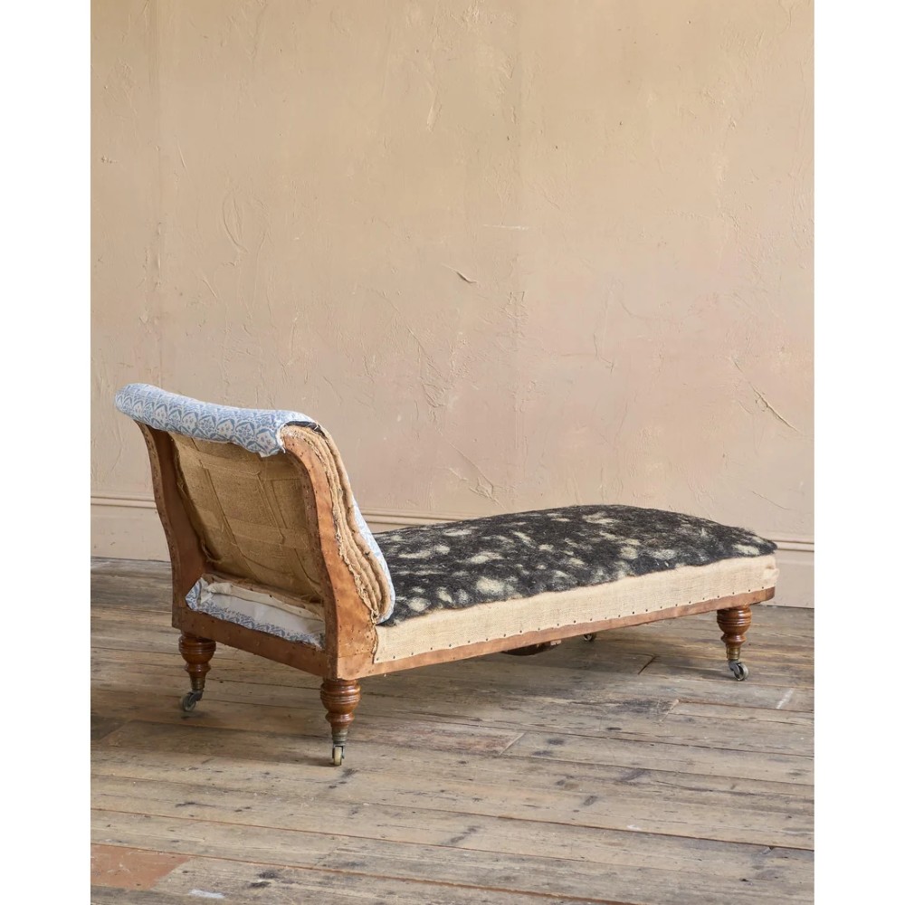 A 19th-century upholstered chaise longue with turned wooden legs on brass castors, patterned fabric backrest, hessian base, and cream bolster cushion. View IX