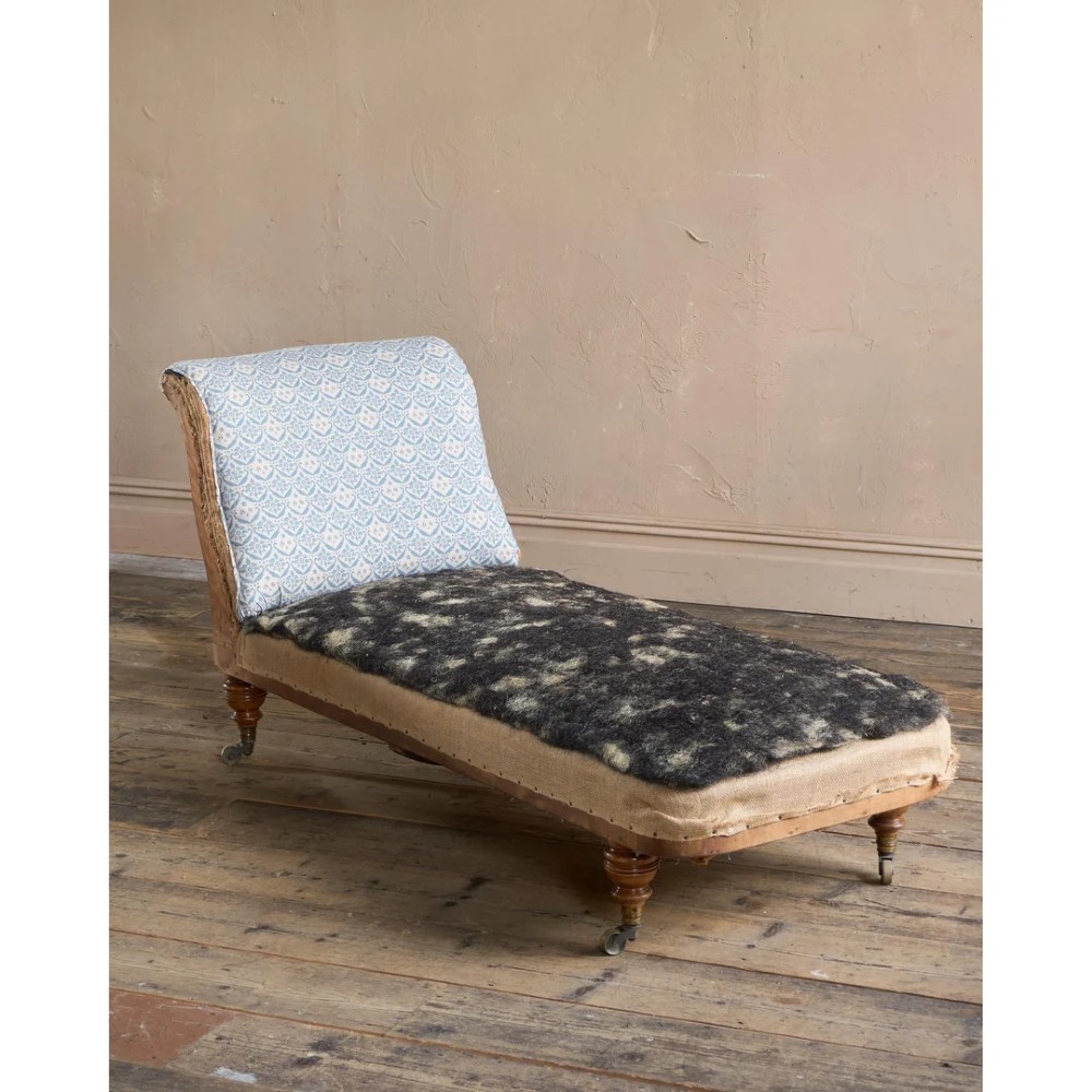 A 19th-century upholstered chaise longue with turned wooden legs on brass castors, patterned fabric backrest, hessian base, and cream bolster cushion. View XI