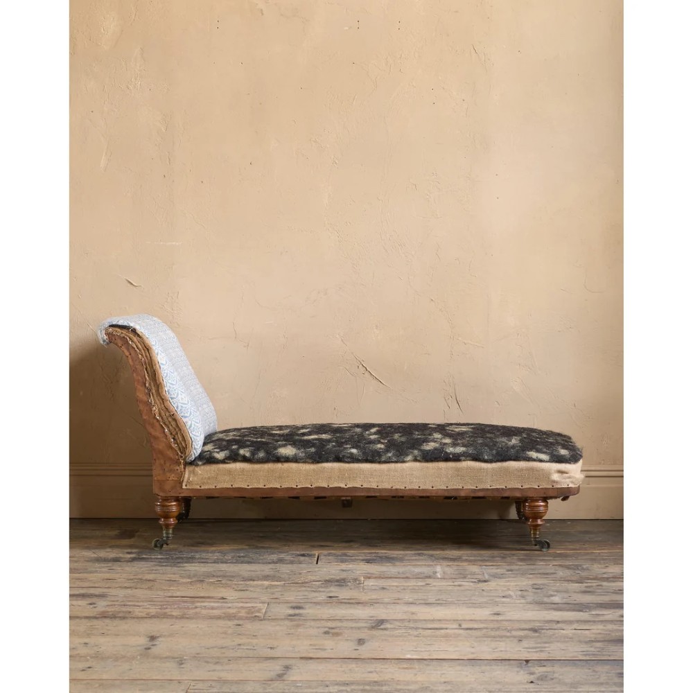 A 19th-century upholstered chaise longue with turned wooden legs on brass castors, patterned fabric backrest, hessian base, and cream bolster cushion. View XII