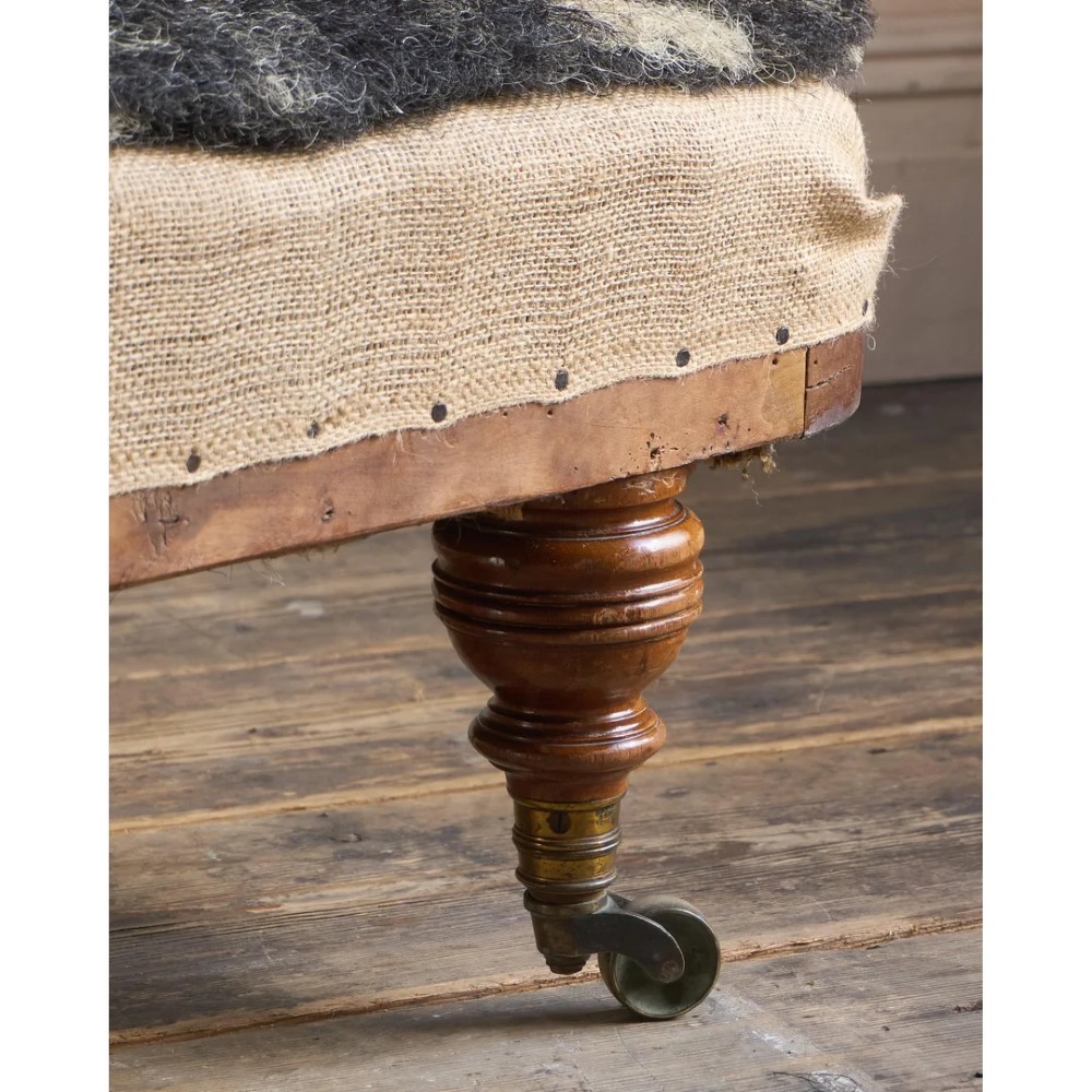A 19th-century upholstered chaise longue with turned wooden legs on brass castors, patterned fabric backrest, hessian base, and cream bolster cushion. View XIV