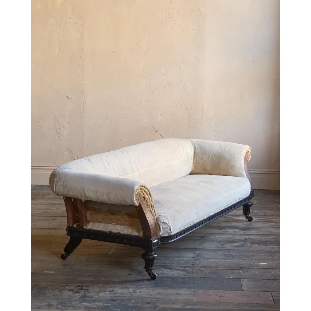 An antique Aesthetic Movement Chesterfield sofa featuring off-white upholstery, rolled arms, a dark carved timber frame, and turned legs with castors. View II