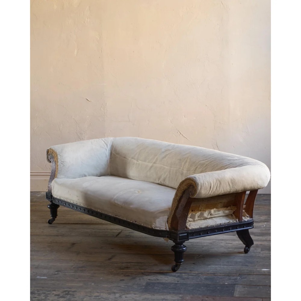 An antique Aesthetic Movement Chesterfield sofa featuring off-white upholstery, rolled arms, a dark carved timber frame, and turned legs with castors. View III