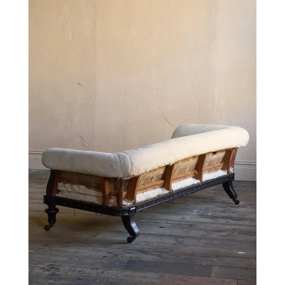 An antique Aesthetic Movement Chesterfield sofa featuring off-white upholstery, rolled arms, a dark carved timber frame, and turned legs with castors. View IV