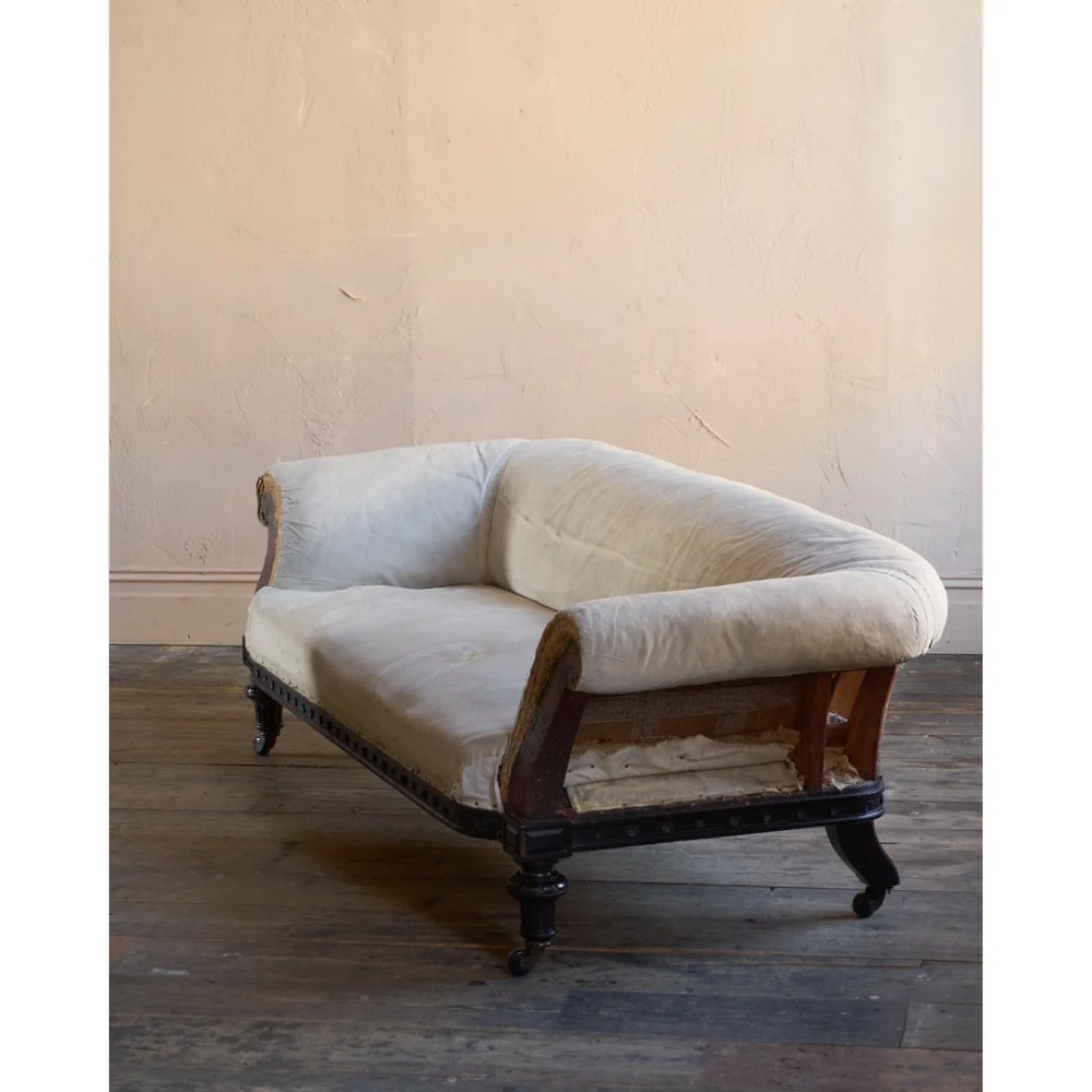 An antique Aesthetic Movement Chesterfield sofa featuring off-white upholstery, rolled arms, a dark carved timber frame, and turned legs with castors. View V