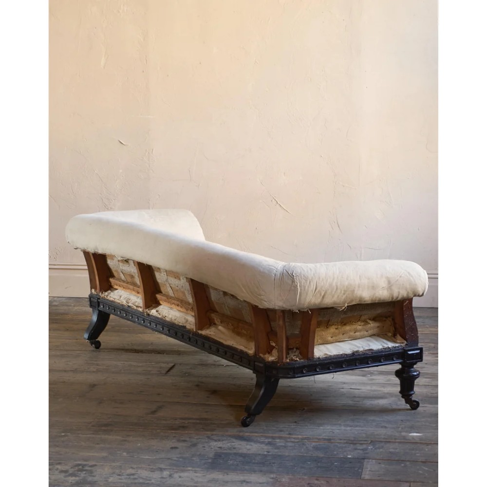 An antique Aesthetic Movement Chesterfield sofa featuring off-white upholstery, rolled arms, a dark carved timber frame, and turned legs with castors. View VI