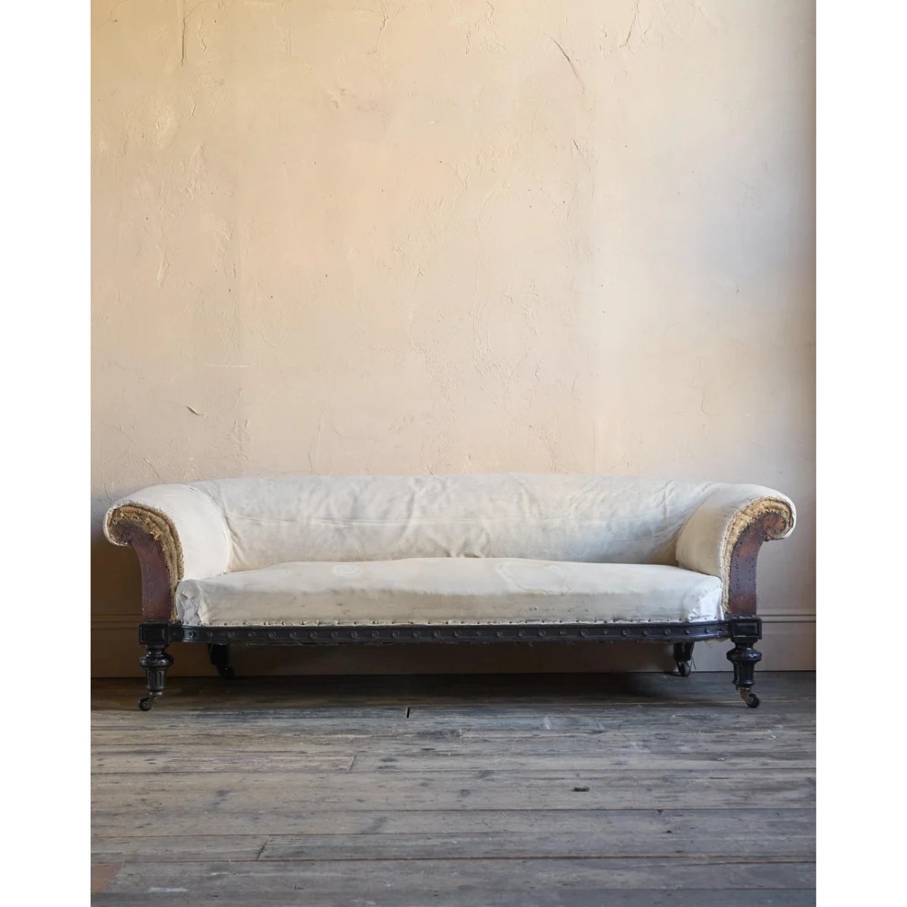 An antique Aesthetic Movement Chesterfield sofa featuring off-white upholstery, rolled arms, a dark carved timber frame, and turned legs with castors. View VII