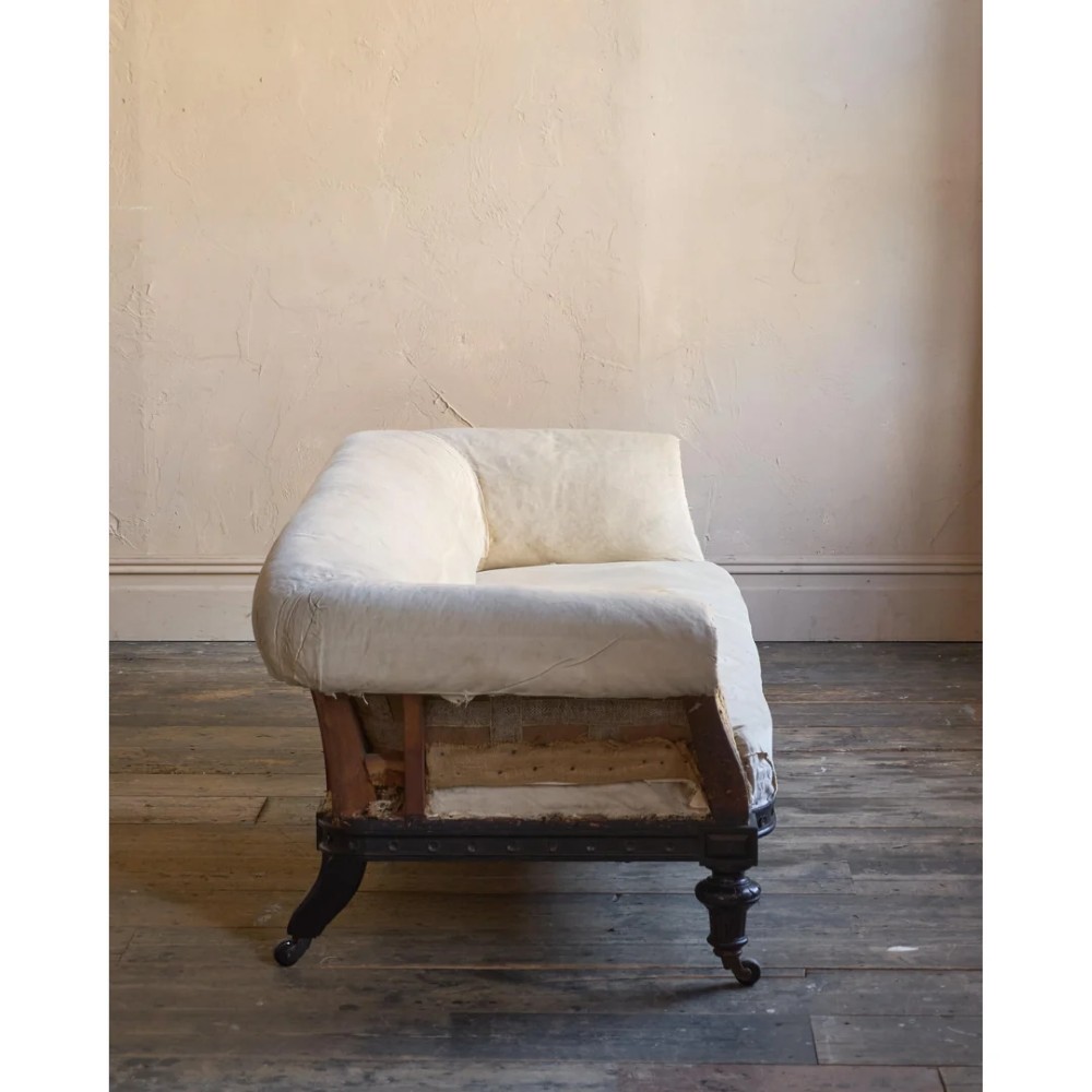 An antique Aesthetic Movement Chesterfield sofa featuring off-white upholstery, rolled arms, a dark carved timber frame, and turned legs with castors. View VIII
