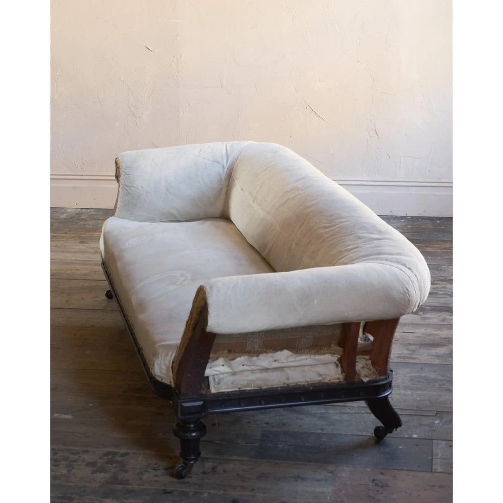 An antique Aesthetic Movement Chesterfield sofa featuring off-white upholstery, rolled arms, a dark carved timber frame, and turned legs with castors. View IX