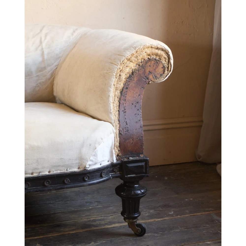 An antique Aesthetic Movement Chesterfield sofa featuring off-white upholstery, rolled arms, a dark carved timber frame, and turned legs with castors. View XI