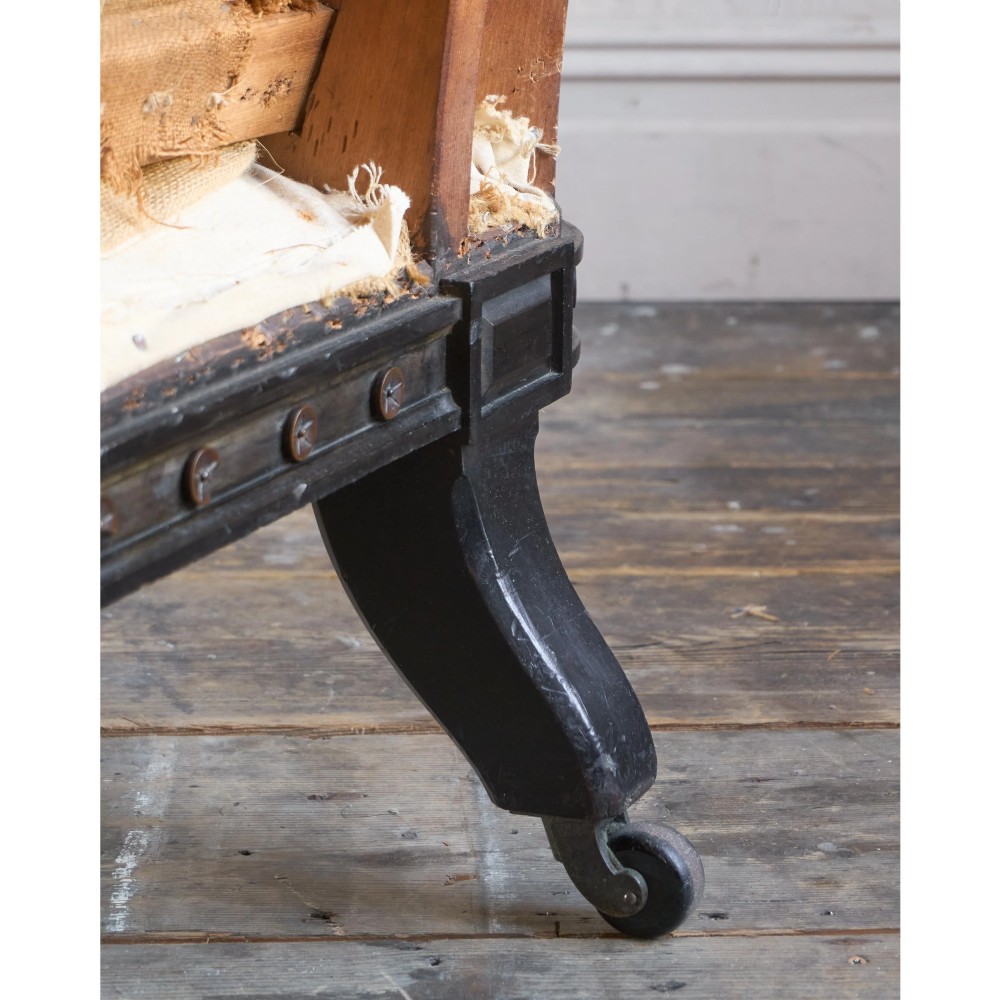 An antique Aesthetic Movement Chesterfield sofa featuring off-white upholstery, rolled arms, a dark carved timber frame, and turned legs with castors. View XIII