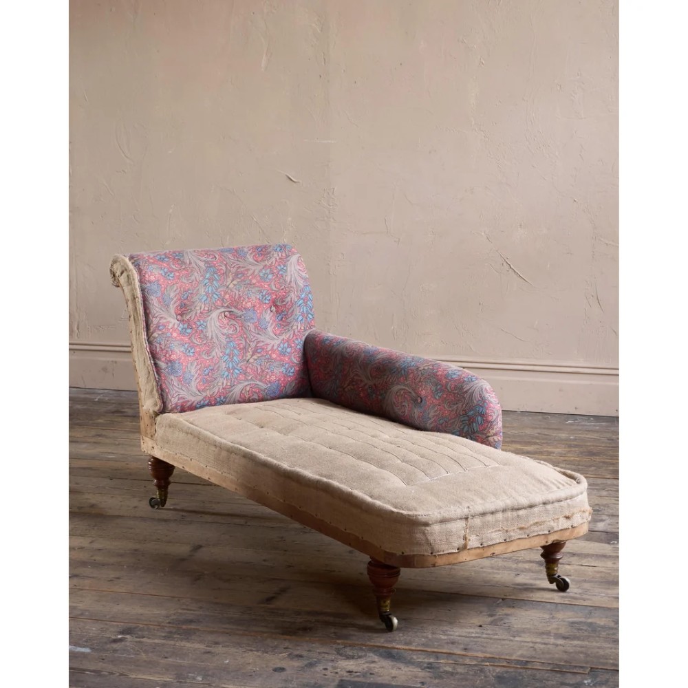 An antique Victorian chaise longue by Howard and Sons featuring patterned fabric upholstery, a single armrest, turned legs, and brass castors.