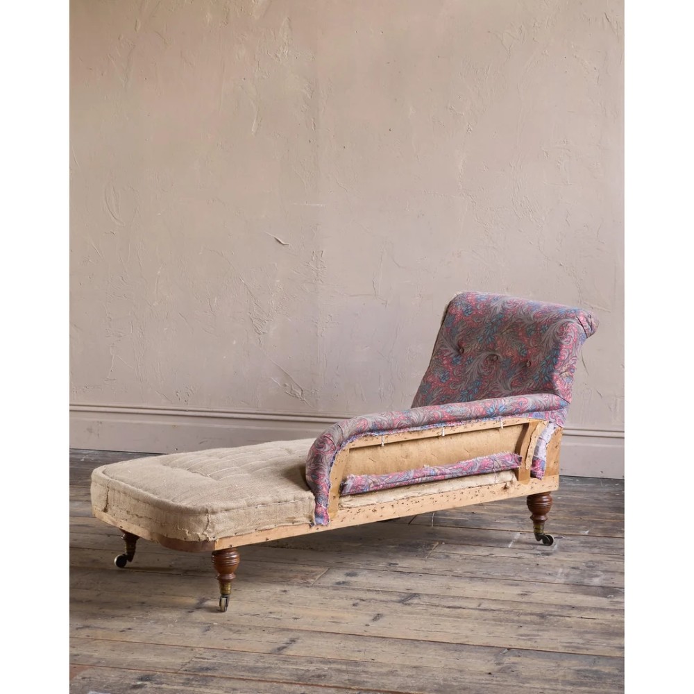 An antique Victorian chaise longue by Howard and Sons featuring patterned fabric upholstery, a single armrest, turned legs, and brass castors. View II