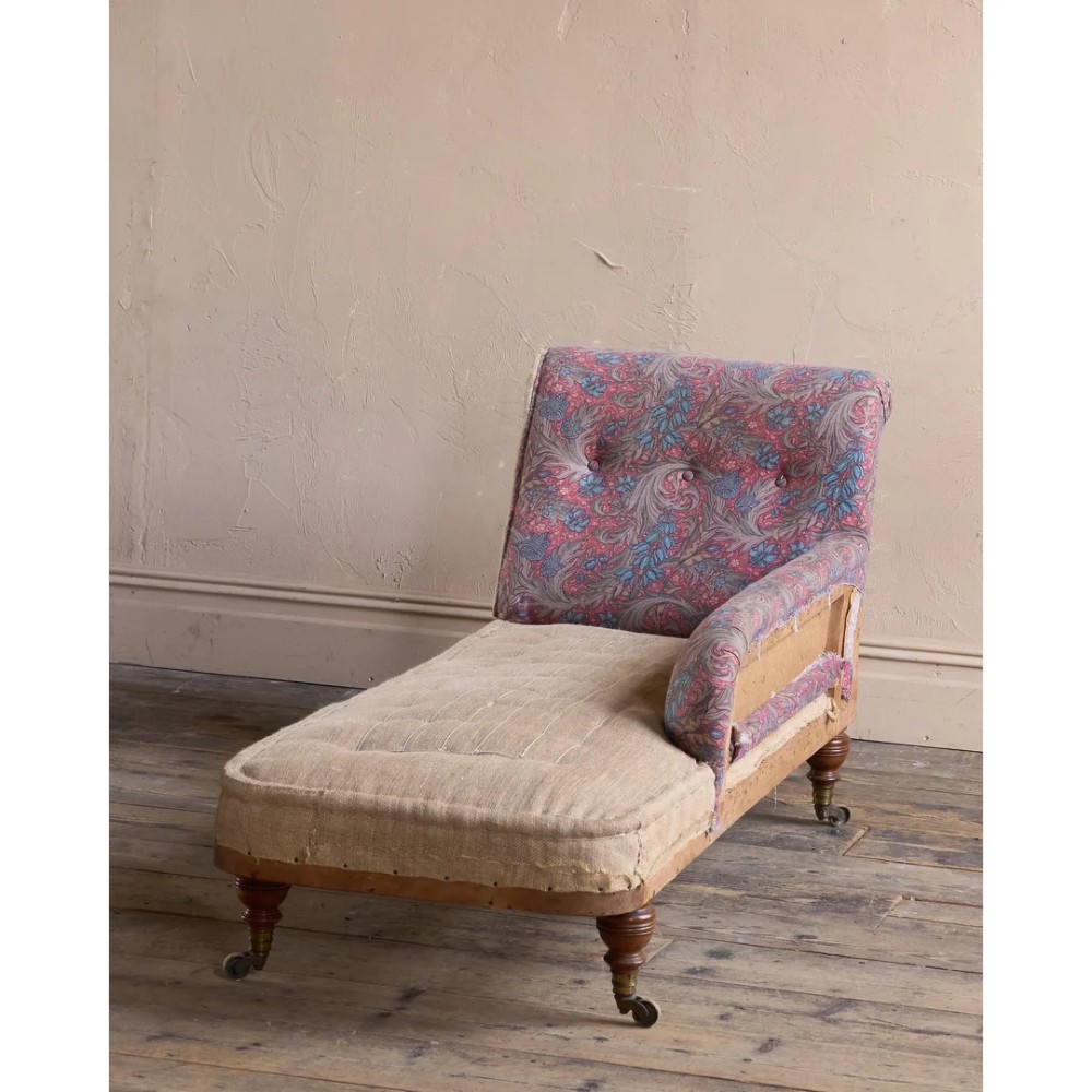 An antique Victorian chaise longue by Howard and Sons featuring patterned fabric upholstery, a single armrest, turned legs, and brass castors. View V