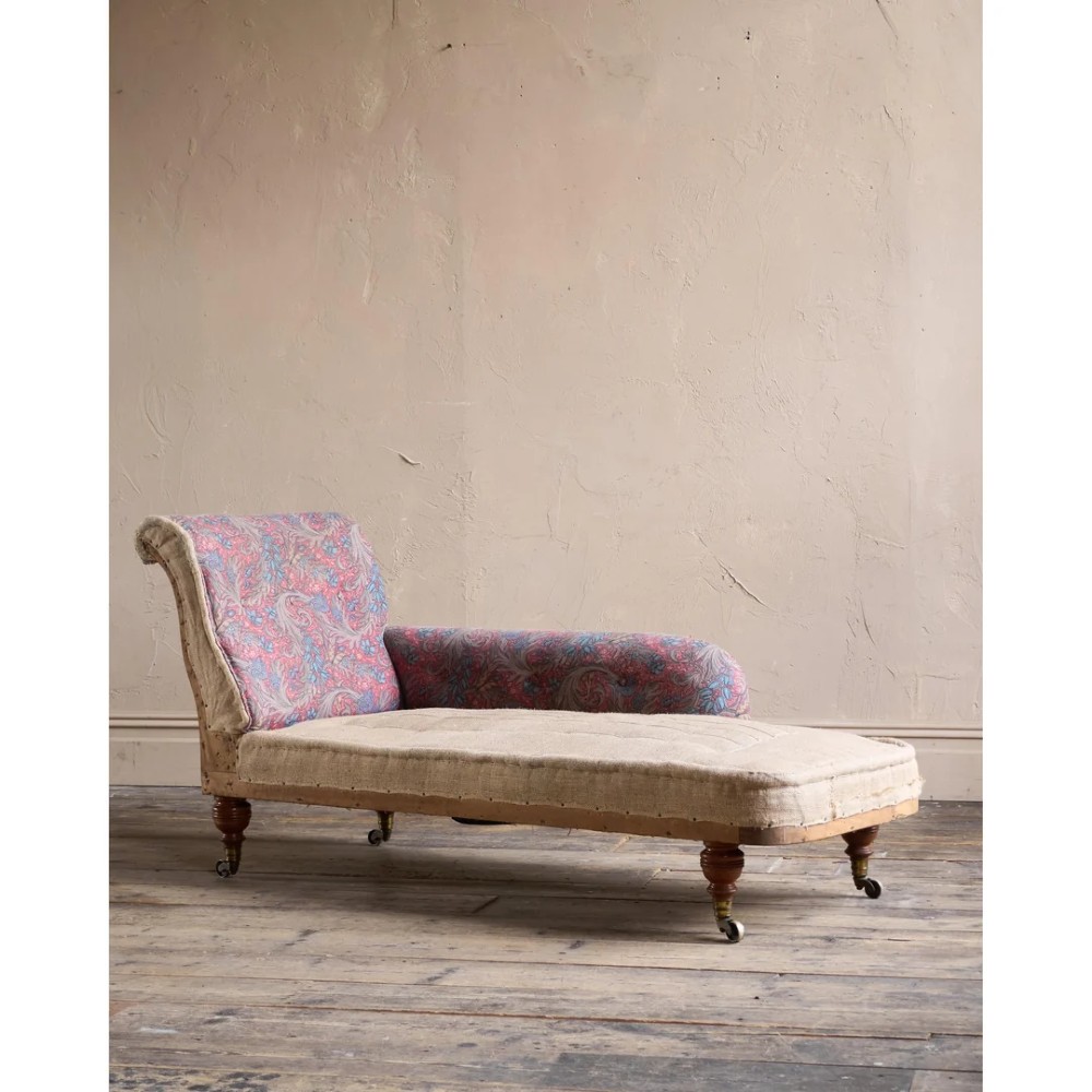 An antique Victorian chaise longue by Howard and Sons featuring patterned fabric upholstery, a single armrest, turned legs, and brass castors. View VI