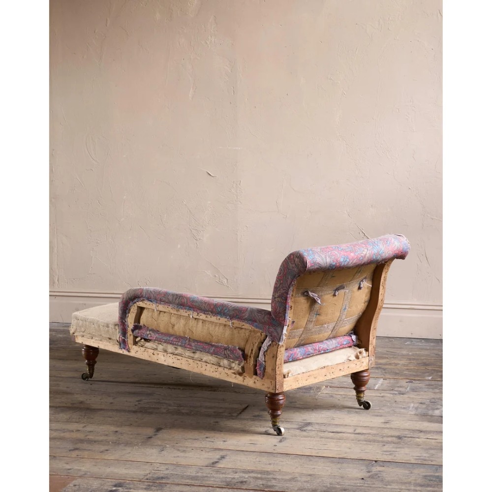 An antique Victorian chaise longue by Howard and Sons featuring patterned fabric upholstery, a single armrest, turned legs, and brass castors. View VII
