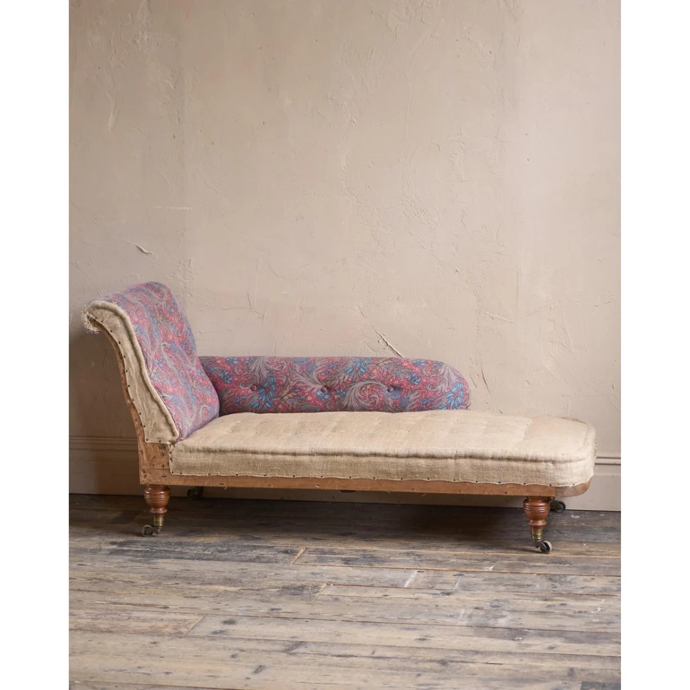 An antique Victorian chaise longue by Howard and Sons featuring patterned fabric upholstery, a single armrest, turned legs, and brass castors. View X