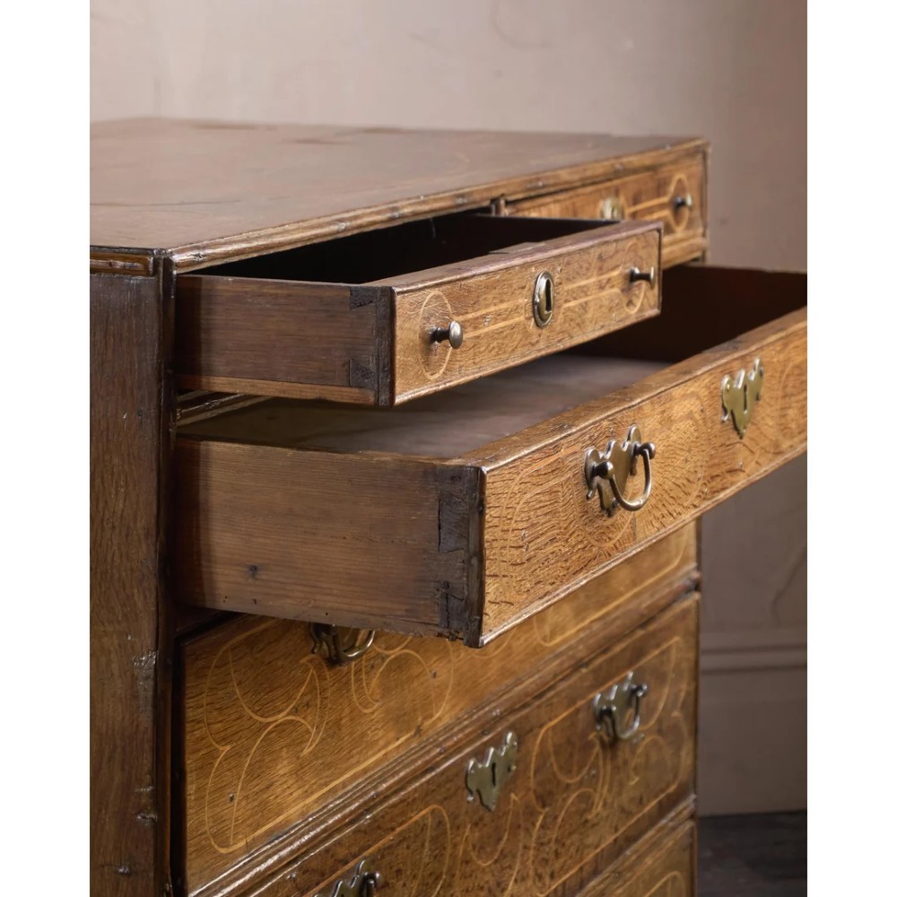 A late 17th-century William and Mary oak chest of drawers featuring geometric scrollwork inlay and brass drop handles. View X