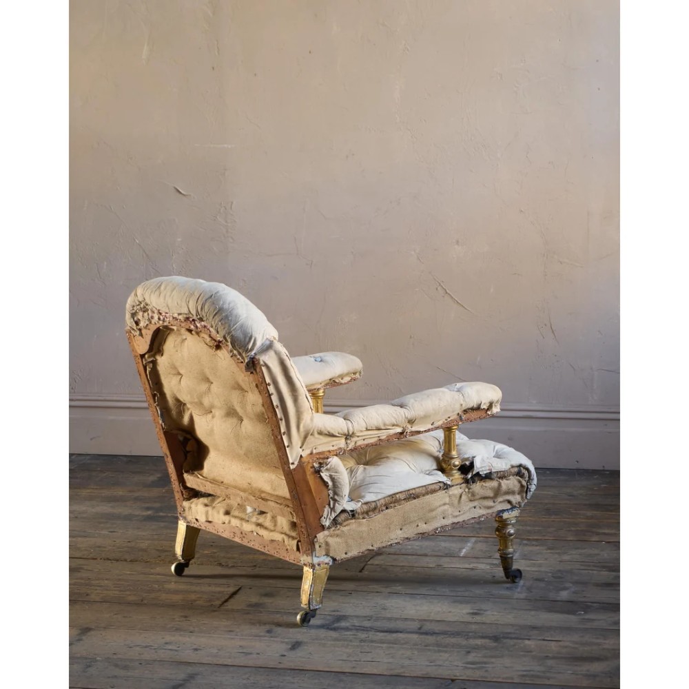 A Victorian open armchair upholstered in off-white calico fabric with deep buttoning, padded armrests, turned legs, and brass castors. View V