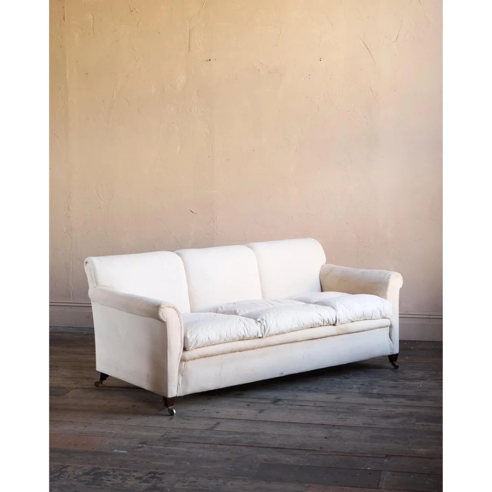 An Edwardian upholstered sofa featuring off-white neutral fabric, low padded armrests, deep seat cushions, and a pleated base skirt. View II