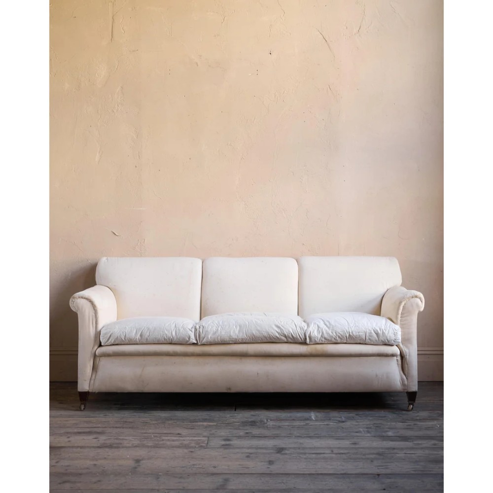 An Edwardian upholstered sofa featuring off-white neutral fabric, low padded armrests, deep seat cushions, and a pleated base skirt. View III