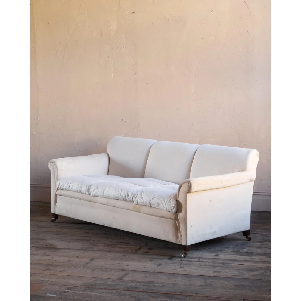 An Edwardian upholstered sofa featuring off-white neutral fabric, low padded armrests, deep seat cushions, and a pleated base skirt. View IV