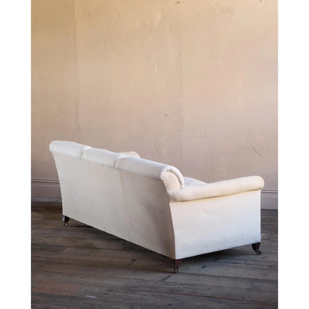 An Edwardian upholstered sofa featuring off-white neutral fabric, low padded armrests, deep seat cushions, and a pleated base skirt. View V