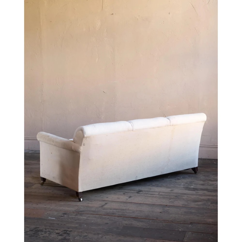 An Edwardian upholstered sofa featuring off-white neutral fabric, low padded armrests, deep seat cushions, and a pleated base skirt. View VI