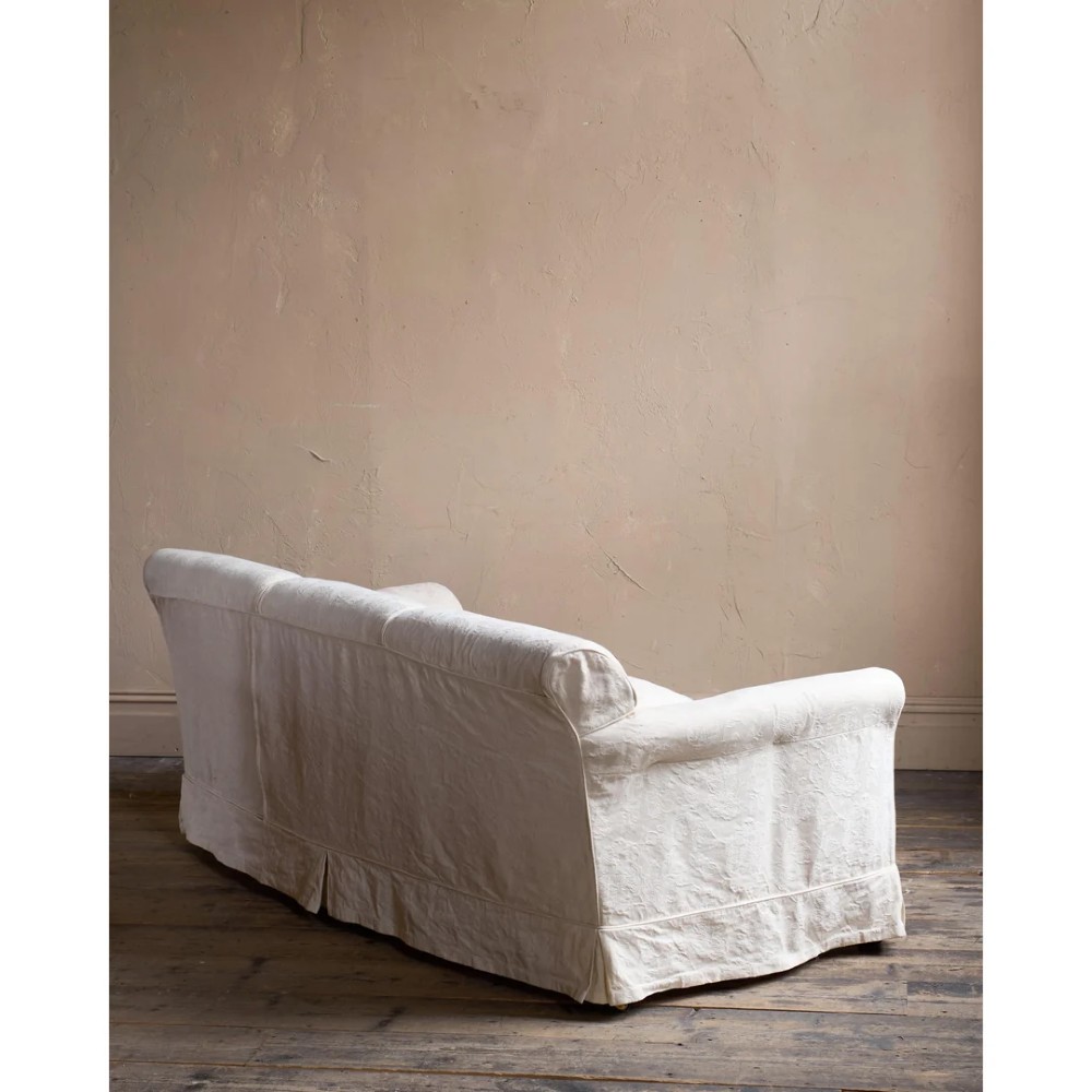 An Edwardian upholstered sofa featuring off-white neutral fabric, low padded armrests, deep seat cushions, and a pleated base skirt. View VIII