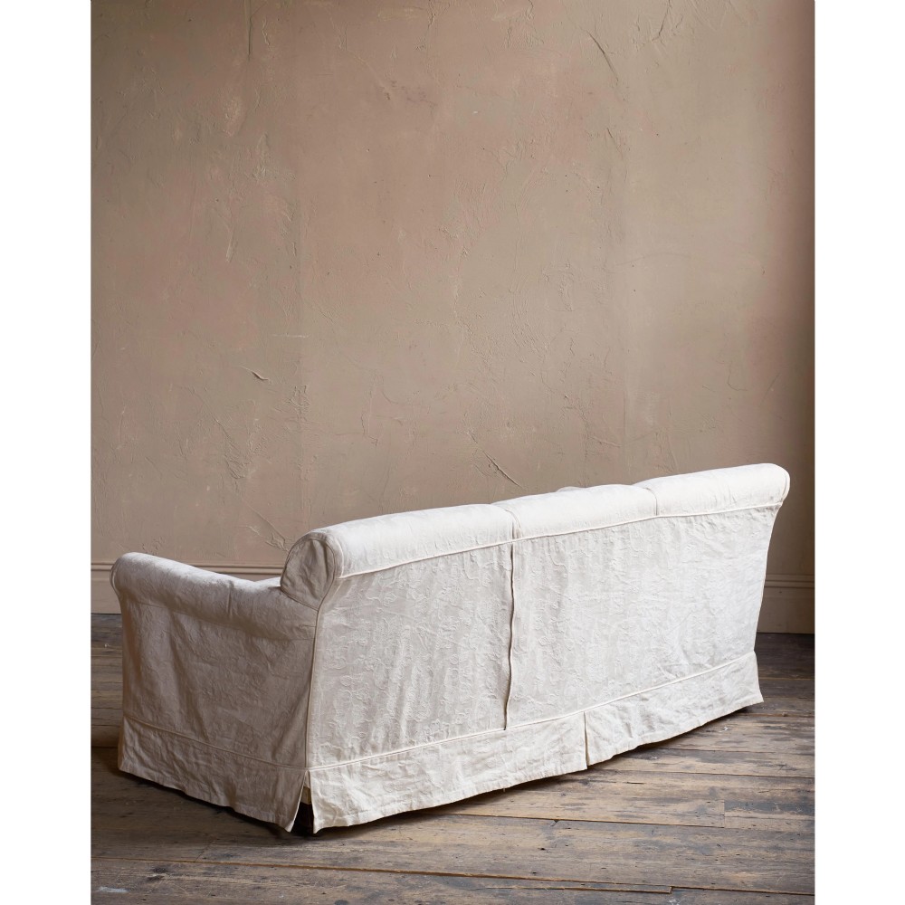 An Edwardian upholstered sofa featuring off-white neutral fabric, low padded armrests, deep seat cushions, and a pleated base skirt. View XI