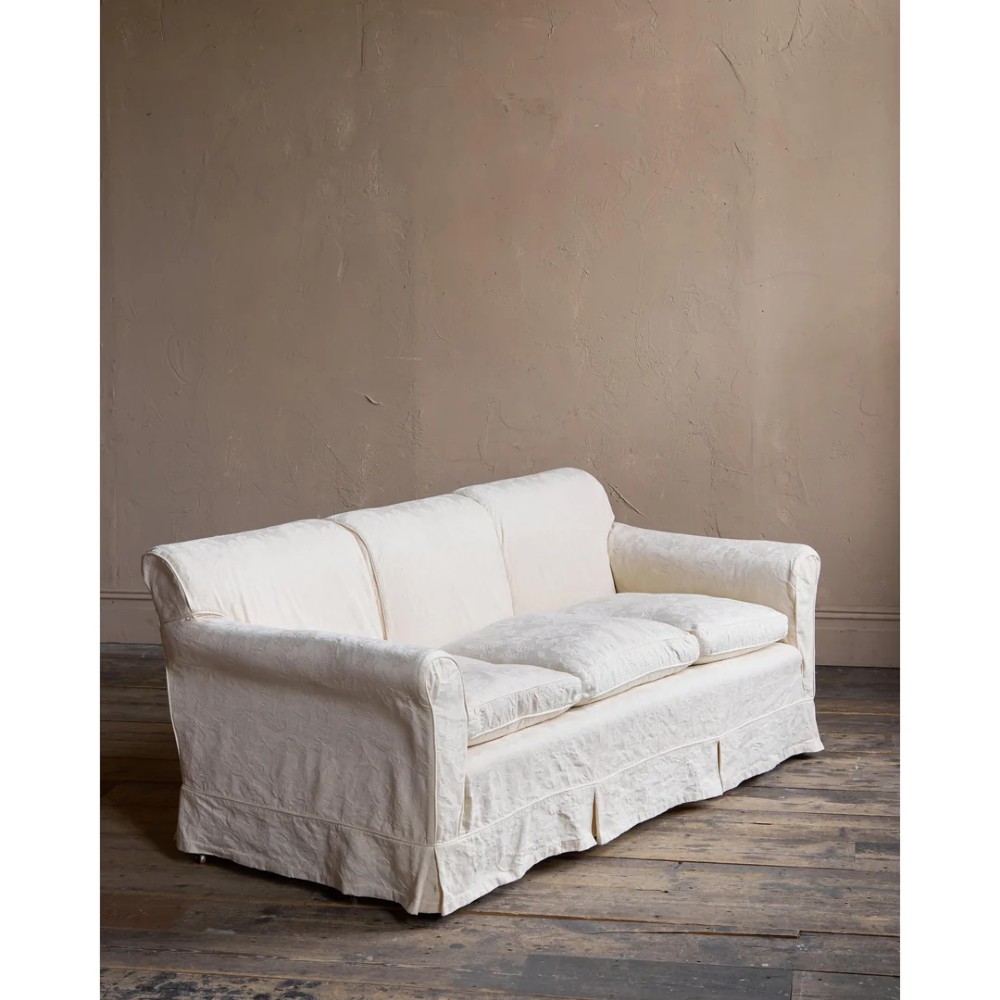 An Edwardian upholstered sofa featuring off-white neutral fabric, low padded armrests, deep seat cushions, and a pleated base skirt. View XII