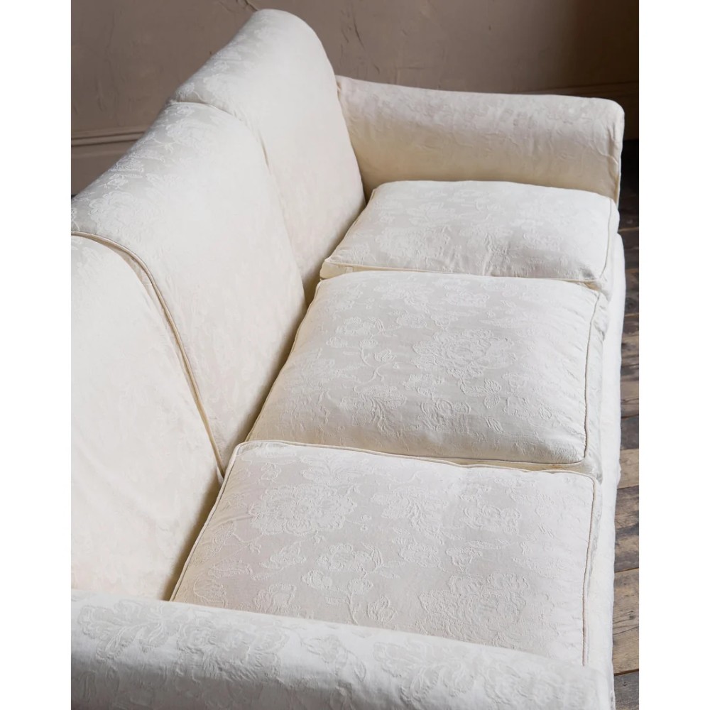 An Edwardian upholstered sofa featuring off-white neutral fabric, low padded armrests, deep seat cushions, and a pleated base skirt. View XIII