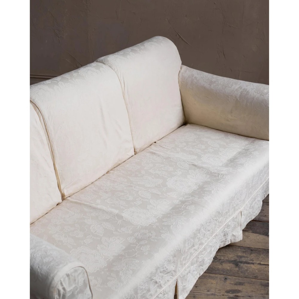 An Edwardian upholstered sofa featuring off-white neutral fabric, low padded armrests, deep seat cushions, and a pleated base skirt. View XIV