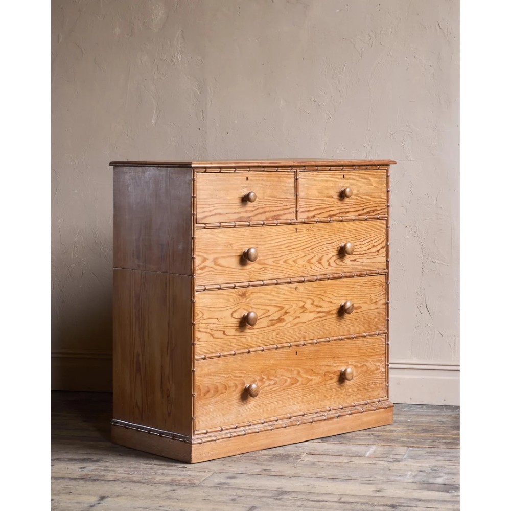 A Victorian pitch pine chest of drawers featuring two short over three long drawers framed with carved faux bamboo mouldings and turned wooden knobs.