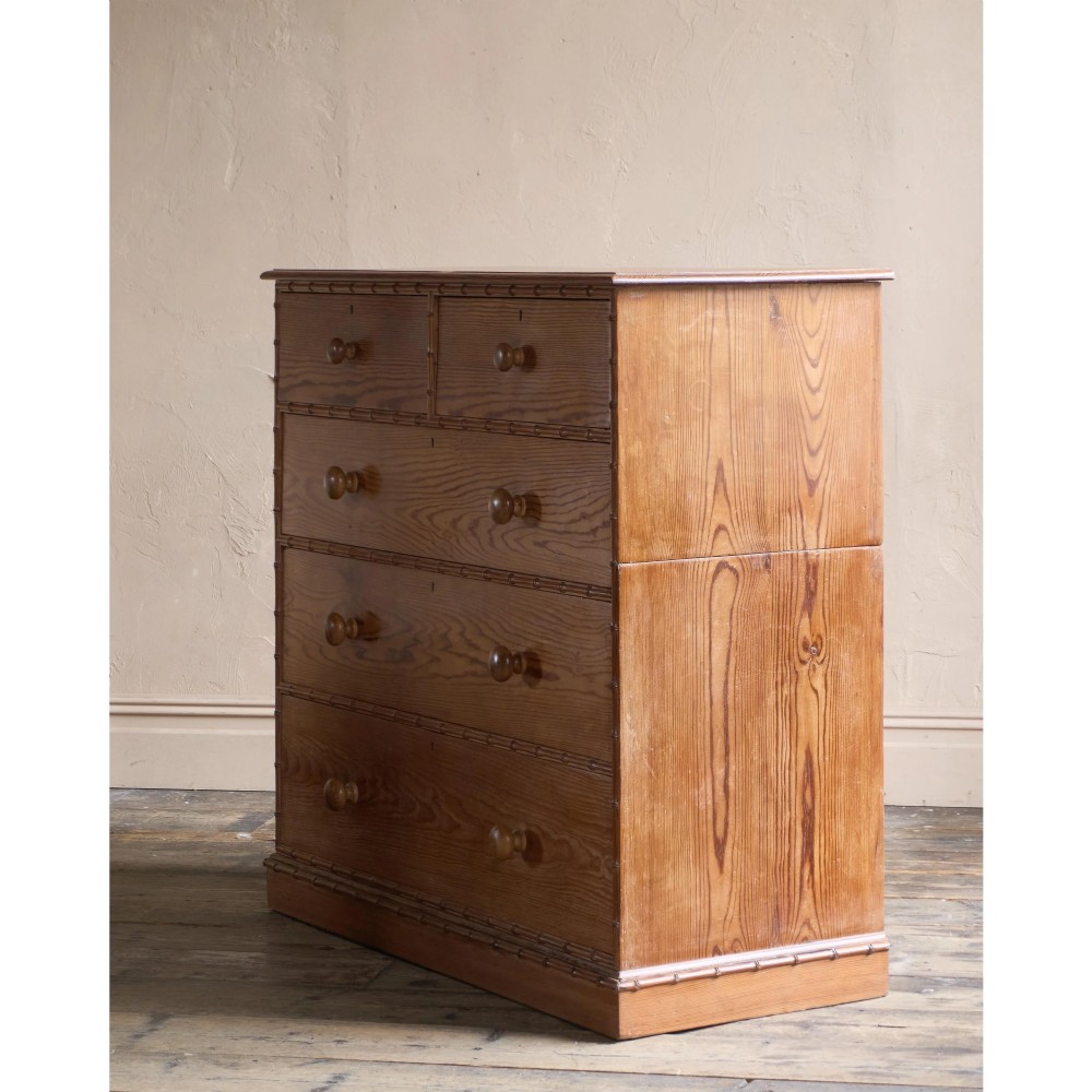 A Victorian pitch pine chest of drawers featuring two short over three long drawers framed with carved faux bamboo mouldings and turned wooden knobs. View IV