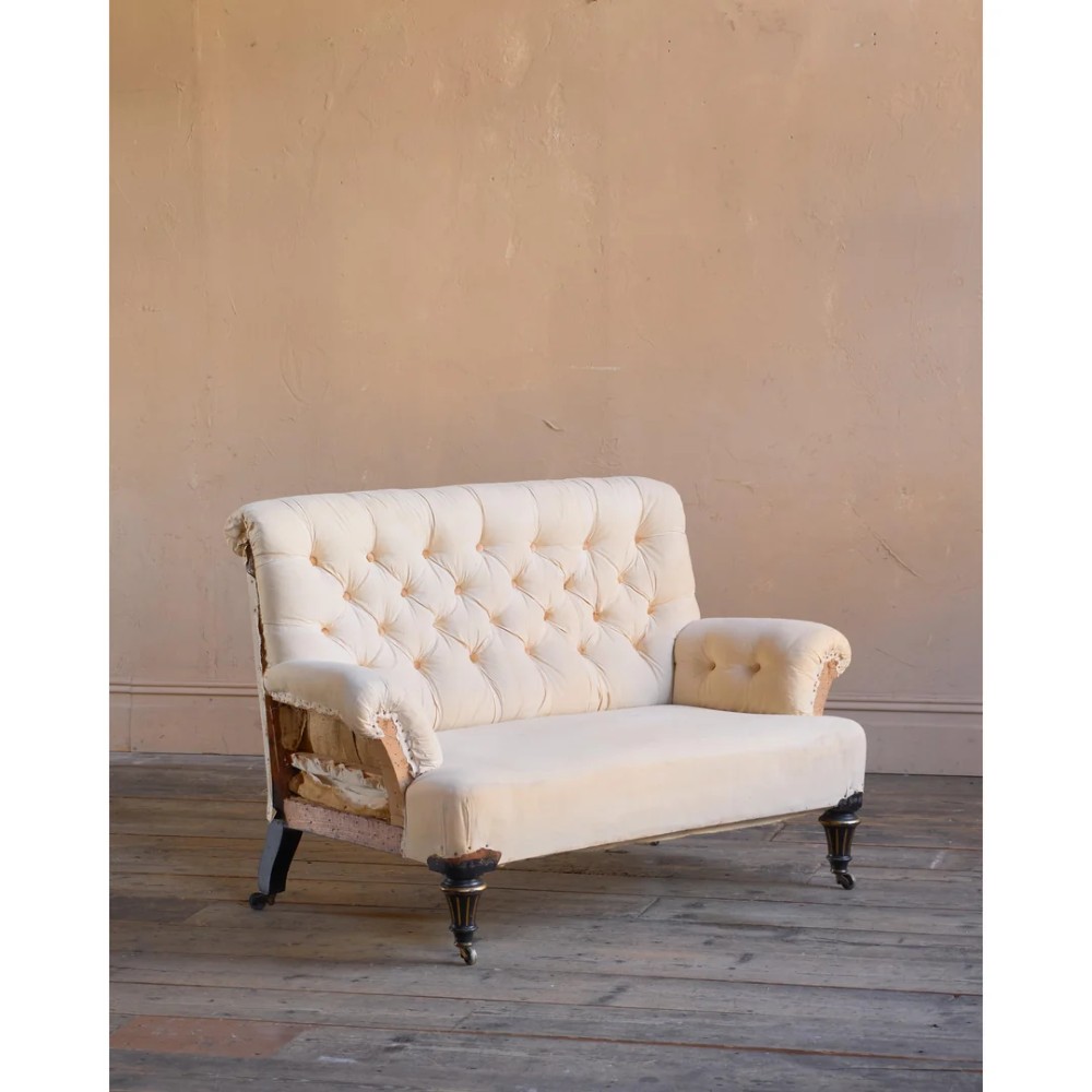 A Victorian two-seater sofa featuring deep button-tufted off-white calico upholstery, scroll arms, and turned front legs with brass castors. View II