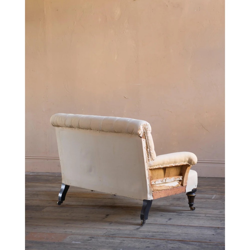 A Victorian two-seater sofa featuring deep button-tufted off-white calico upholstery, scroll arms, and turned front legs with brass castors. View III