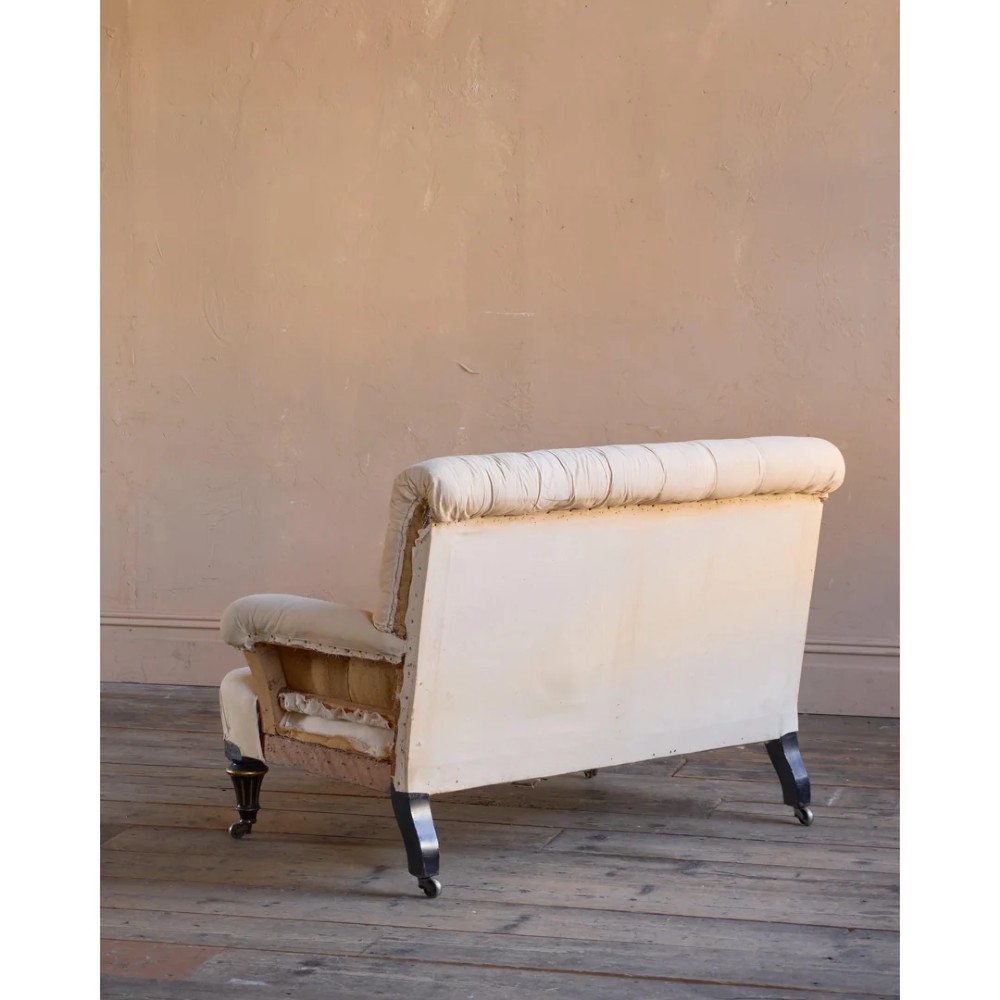 A Victorian two-seater sofa featuring deep button-tufted off-white calico upholstery, scroll arms, and turned front legs with brass castors. View IV