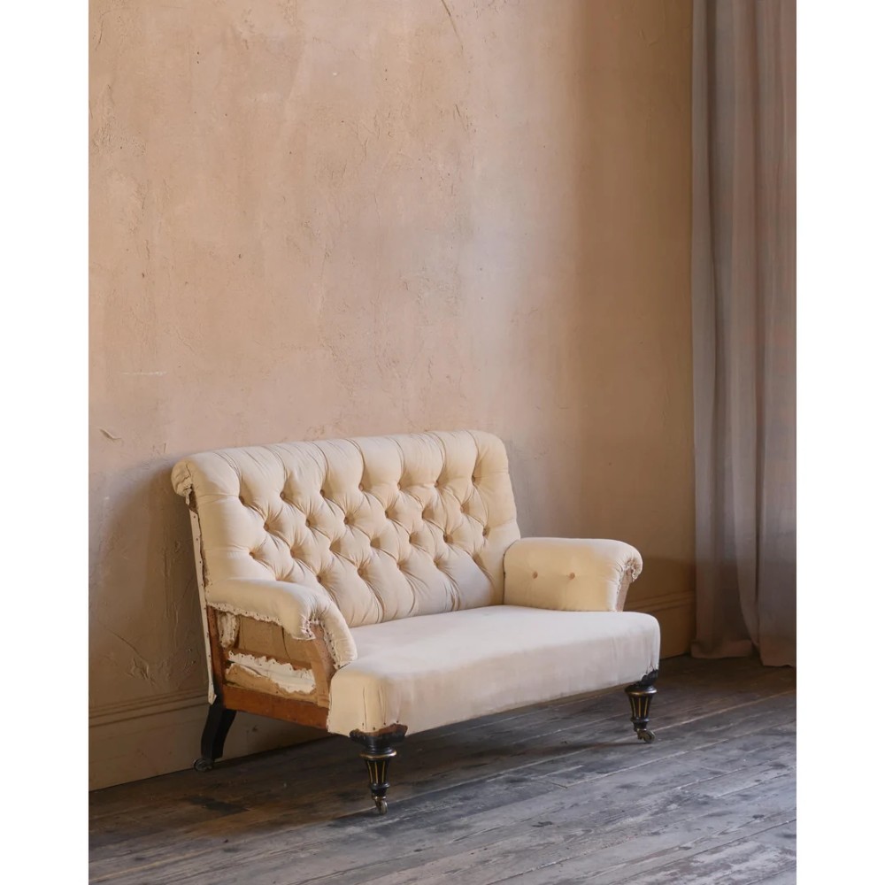 A Victorian two-seater sofa featuring deep button-tufted off-white calico upholstery, scroll arms, and turned front legs with brass castors. View VI