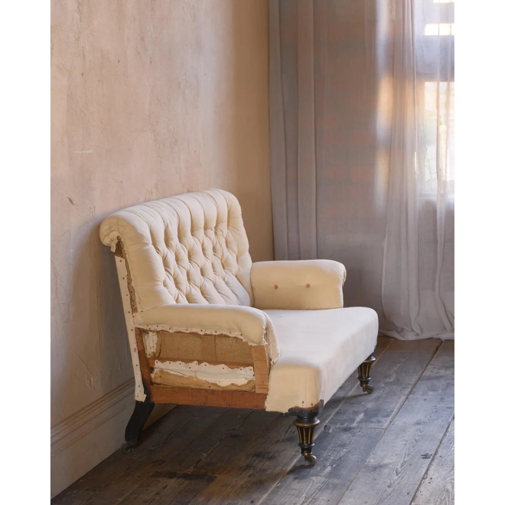 A Victorian two-seater sofa featuring deep button-tufted off-white calico upholstery, scroll arms, and turned front legs with brass castors. View VII